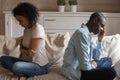 Unhappy african couple ignoring each other sitting separately on couch