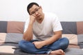 Unhappy Asian man sitting and thinking on his sofa at home in the living room, sad expression Royalty Free Stock Photo
