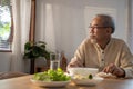 Unhappy Asian Senior older man sit alone, eat foods on table in house. Depressed mature attractive elderly retired grandfather