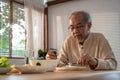 Unhappy Asian Senior older man sit alone, eat foods on table in house. Depressed mature attractive elderly retired grandfather
