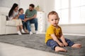 Unhappy baby sitting alone on floor while parents spending time with his elder brother. Jealousy in family Royalty Free Stock Photo
