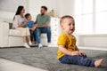 Unhappy baby sitting alone on floor while parents spending time with his elder brother. Jealousy in family Royalty Free Stock Photo