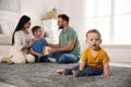 Unhappy baby sitting alone on floor while parents spending time with his elder brother. Jealousy in family Royalty Free Stock Photo