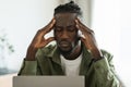 Unhappy black male freelancer touching head, suffering from headache or having issues with work, sitting at desk Royalty Free Stock Photo