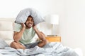 Unhappy black man sitting on bed, covering head with pillow Royalty Free Stock Photo