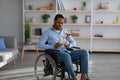 Unhappy black paraplegic sportsman in wheelchair holding trophies, feeling depressed indoors
