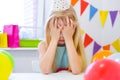 Unhappy blonde caucasian girl is crying near birthday rainbow cake. Festive colorful background. Bad birthday party Royalty Free Stock Photo