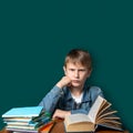 Unhappy boy of European appearance is sitting on the background of the school green board. Teen does not want to school. A stack