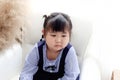 Unhappy chubby Asian girl kid sitting on a white sofa in the living room. Portrait of upset little toddler girl child feeling Royalty Free Stock Photo