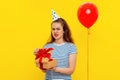 Unhappy confused young woman wears party cone and striped t shirt, opens gift box, feels embarrassed and offended has bad mood Royalty Free Stock Photo