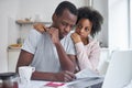 Unhappy couple in trouble. Wife hugs unemployed husband, he looks at papers on table