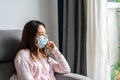 Unhappy depressed thoughtful young asian woman wearing medical mask sitting alone absent-minded at living room at home Royalty Free Stock Photo