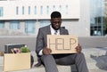 Unhappy despaired black businessman lost work holding placard with word HELP, sitting on stairs near business center Royalty Free Stock Photo