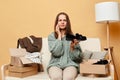 Unhappy disappointed woman wearing knitted sweater with ordered clothes in boxes sitting at home on couch against beige wall Royalty Free Stock Photo