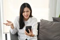 Unhappy and dissatisfied Asian woman sitting on sofa, receiving unreasonable news or message