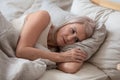 Unhappy elderly woman lying in bed thinking