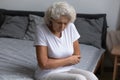 Unhappy elderly woman sitting on bed, feeling strong belly ache Royalty Free Stock Photo