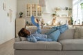 Unhappy exhausted and overheated young African woman lying on sofa at home waving fan to cool down Royalty Free Stock Photo