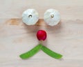 Unhappy face made with garlic, radish and snow peas on a wood background