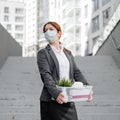 Unhappy fired masked woman is standing in the street with a box of personal items from the desktop. An unemployed