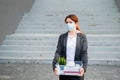 Unhappy fired masked woman is standing in the street with a box of personal items from the desktop. An unemployed