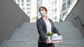 Unhappy fired masked woman is standing in the street with a box of personal items from the desktop. An unemployed