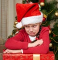 Unhappy girl crying near christmas tree, dressed in red and santa hat Royalty Free Stock Photo