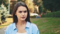 Unhappy girl frawns, being on blurred summer park background. Close up. Copy space. 4K.