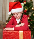 Unhappy girl shed tears near christmas tree, dressed in red and santa hat Royalty Free Stock Photo