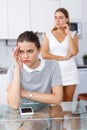 Unhappy girl sitting at table after quarrel, woman friend on backround