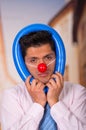 Unhappy handsome businessman with red plastic nose with a blue ballon aroun his head Royalty Free Stock Photo