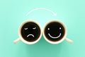 Unhappy and happy smileys faces over cpffee cups. concept of mindset and emotions Royalty Free Stock Photo