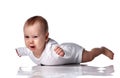 Unhappy infant baby boy toddler in diaper and white bodysuit is lying on floor on his stomach and crying Royalty Free Stock Photo