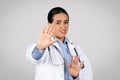 Unhappy latin female doctor making stop gesture with hands, disgust sign, medicine problems, fight against disease
