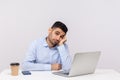 Unhappy lazy inefficient man employee sitting office workplace with laptop on desk, looking disinterested