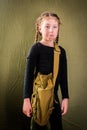 An unhappy little girl in a black leotard and a military bag over her shoulder poses in the Studio. A sad child dressed in