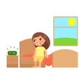 Unhappy little girl sits on the bed and is angry at the sound of the alarm clock. Royalty Free Stock Photo