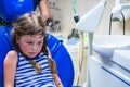 An unhappy little girl is sitting in a dental chair. The child, sweaty from excitement, is in a stomatological clinic