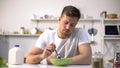 Unhappy lonely man looking with disgust at food in bowl, lack of appetite