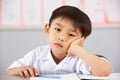 Unhappy Male Student Working At Desk In School