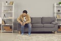 Unhappy young man sitting on couch at home and suffering from severe pain in knee joint Royalty Free Stock Photo