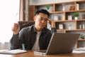 Unhappy mature asian guy analyzes data on laptop, presses hand to head, suffers from problems in business