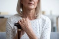 Unhappy mature woman holding hands on walking stick close up