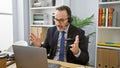 Unhappy, middle aged man with grey hair arguing on video call at office while working Royalty Free Stock Photo