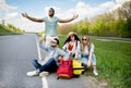 Unhappy millennial tourists sitting on roadside, cannot catch car, waiting for too long, having no smartphone connection Royalty Free Stock Photo