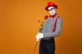 Unhappy mime man with white face in red hat and striped t-shirt holding rose on empty orange background Royalty Free Stock Photo