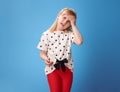 Unhappy modern child in red pants on blue having headache