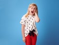 Unhappy modern girl in red pants on blue with earache