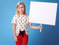 Unhappy modern girl in red pants on blue showing blank poster