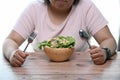 Unhappy overweight woman sitting at a table and looking at a bowl of salad at home.